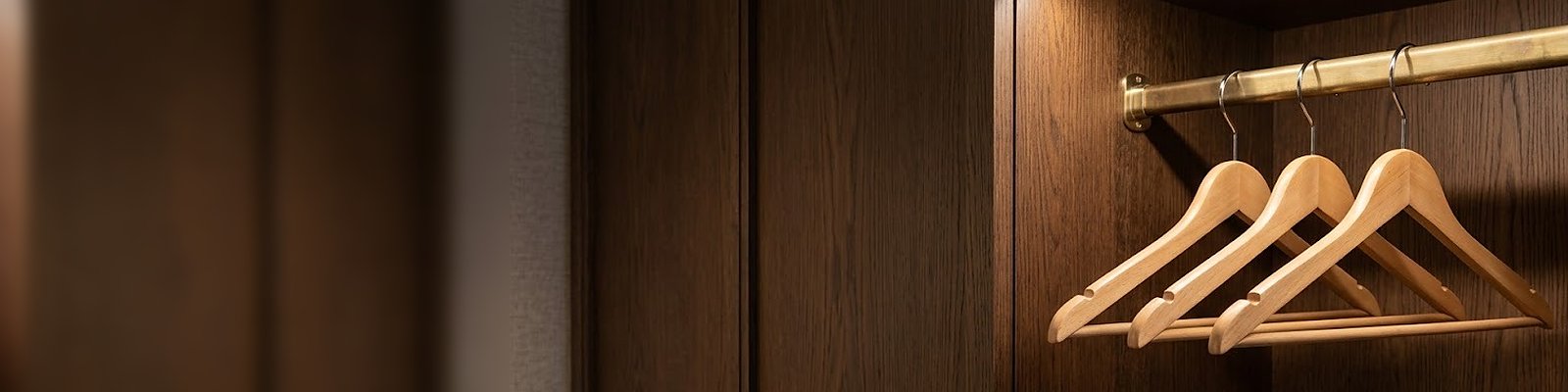 Tres perchas de madera con ganchos cromados en una barra de latón en el armario de una suite de hotel