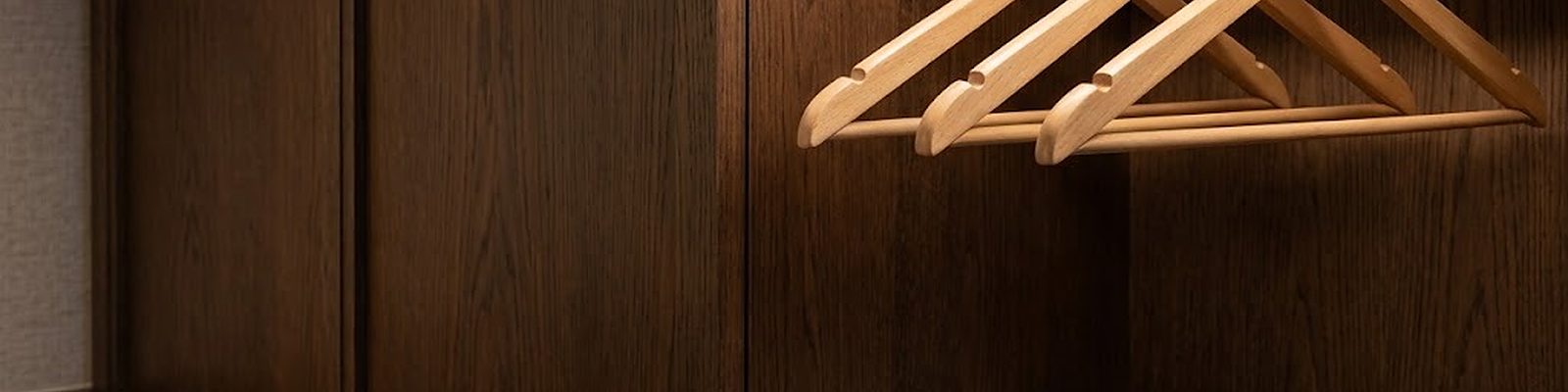 Tres perchas de madera con ganchos cromados en una barra de latón en el armario de una suite de hotel