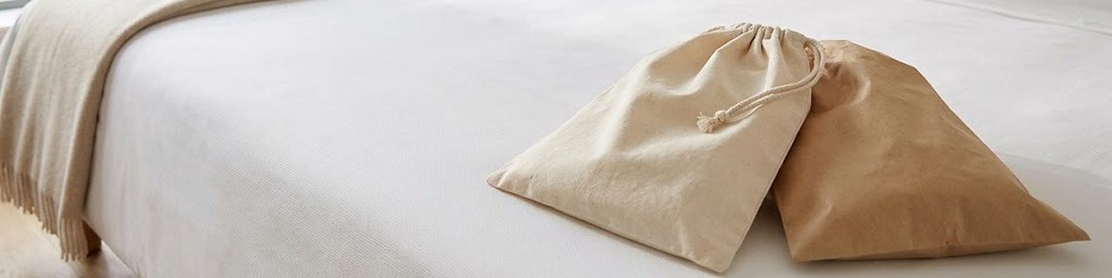 Bolsa de lavandería de algodón con cordón y bolsa de lavandería de papel una junto a otra sobre la colcha de una cama de hotel