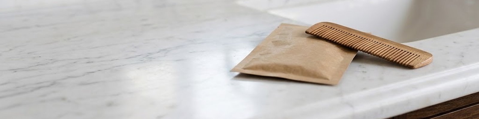 Sachet papier avec un peigne en bois au bord d'une vasque en marbre dans une salle de bain d'hôtel, lumière du matin