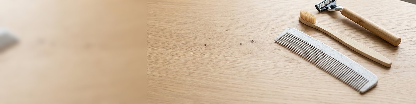 Brosse à dents en bambou, peigne en paille et PP blanc-gris et rasoir à manche bambou sur du chêne clair