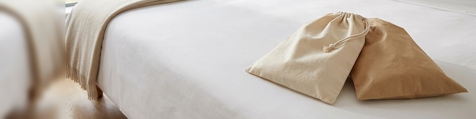 Wäschebeutel aus Baumwolle mit Kordelzug und Wäschebeutel aus Papier nebeneinander auf der Decke eines Hotelbetts